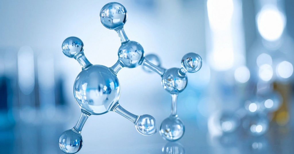 A close-up of a shiny, silver molecular model with connected spheres representing atoms, set against a blurred blue and white laboratory background.
